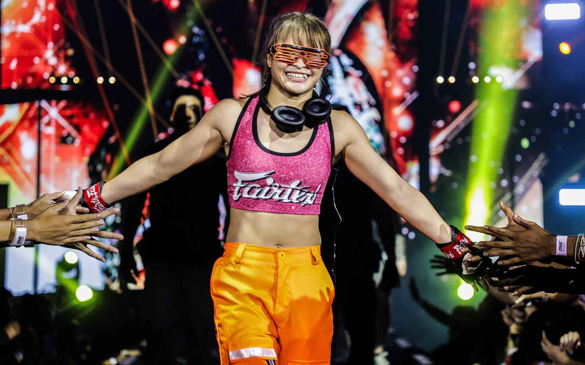 Vechtsportster in een roze Fairtex-top en oranje broek tijdens haar opkomst tussen het publiek.