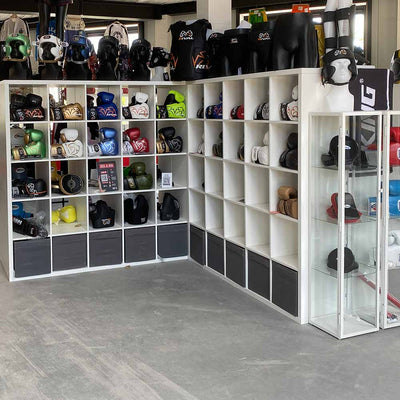 Witte vakkenkasten met Rival-bokshandschoenen, hoofdbeschermers en kleding in de showroom van Fight2Win in Waddinxveen.